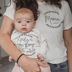 Pode incluir: Uma mulher segurando um beb&ecirc; que est&aacute; vestindo um macac&atilde;o branco com o texto "Only a little boy for such a while" em uma coroa de flores preta. A mulher est&aacute; vestindo uma camiseta branca com o texto "Mama -FOREVER- " em uma coroa de flores preta.