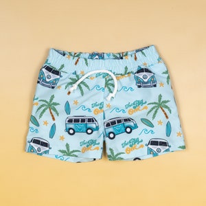 May include: Light blue swimming trunks with a pattern of blue and white surf vans, palm trees, and waves. The text "The Big One" is repeated throughout the pattern.