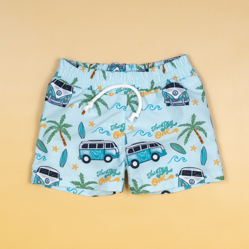 May include: Light blue swimming trunks with a pattern of blue and white surf vans, palm trees, and waves. The text "The Big One" is repeated throughout the pattern.