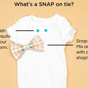 May include: A white onesie with a brown and white plaid bow tie. The onesie has two turquoise snaps on the neckline. The text "What's a SNAP on tie?" is at the top of the image. The text "We embellish blank bodysuits by adding our snap platform." is on the left side of the image. The text "Snap-on ties: Mix and match with any in the shop!" is on the right side of the image.