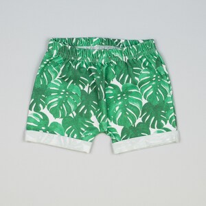 May include: White shorts with a green tropical leaf print. The shorts have a white elastic waistband and a cuffed hem.