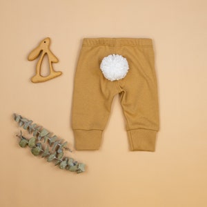 Puede incluir: Leggings de beb&eacute; de color mostaza con una cola de pomp&oacute;n blanco en la parte posterior.