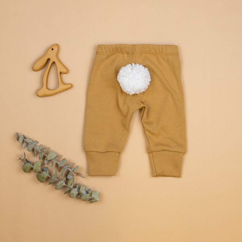 Puede incluir: Leggings de beb&eacute; de color mostaza con una cola de pomp&oacute;n blanco en la parte posterior.
