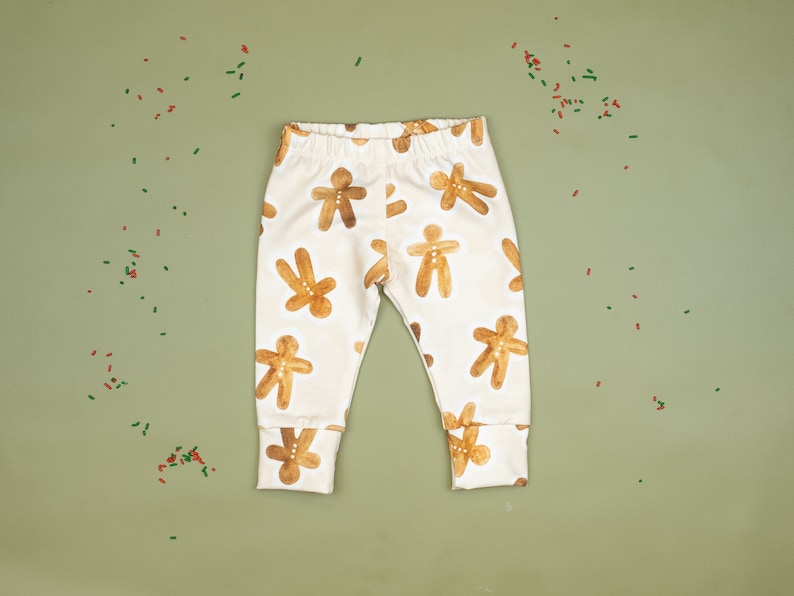 Puede incluir: Leggings de beb&eacute; blancos con un patr&oacute;n de hombre de jengibre. Los leggings tienen un patr&oacute;n de hombre de jengibre marr&oacute;n sobre un fondo blanco.
