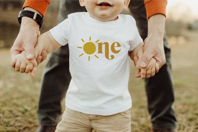 May include: A white t-shirt with a yellow sun and the word "one" in a retro font.