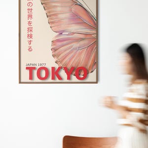 May include: A vintage poster with a butterfly wing design in shades of pink and orange. The poster has the text "昆虫の世界を探検する" in Japanese, which translates to "Explore the world of insects." The poster also has the text "The Rising Wind" and "JAPAN 1977 TOKYO" in red.