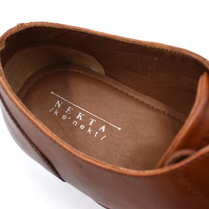 May include: Close-up of the inside of a brown leather shoe with a white label that reads "NEKTA | k.nekt/"