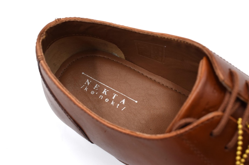 May include: Close-up of the inside of a brown leather shoe with a white label that reads "NEKTA | k.nekt/"