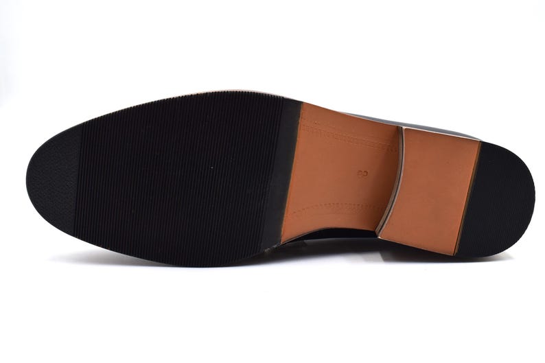 Pode incluir: A sola de um sapato de couro preto com uma sola de couro marrom. A sola tem um padr&atilde;o texturizado e o sapato tem uma ponta arredondada.