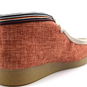 May include: A pair of red canvas shoes with a brown sole and a black and white striped trim around the top.