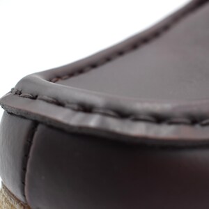 May include: Close-up of the top edge of a brown leather loafer. The leather is stitched with a dark brown thread.