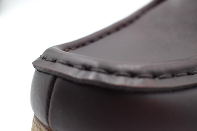 May include: Close-up of the top edge of a brown leather loafer. The leather is stitched with a dark brown thread.