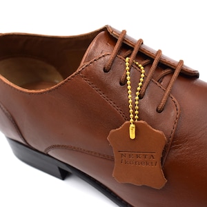 May include: Brown leather lace-up dress shoes with a gold chain attached to a brown leather tag that reads "NEKTA  koneku".