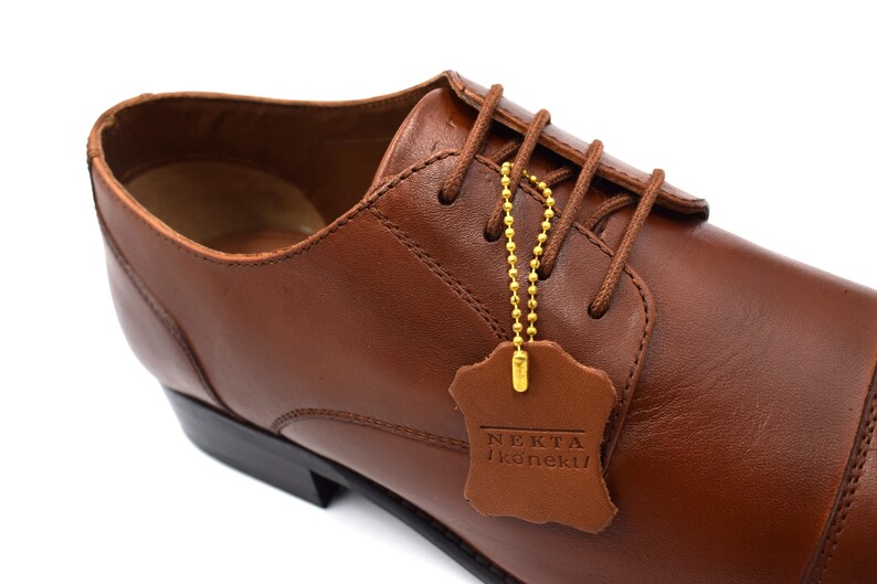 May include: Brown leather lace-up dress shoes with a gold chain attached to a brown leather tag that reads "NEKTA  koneku".