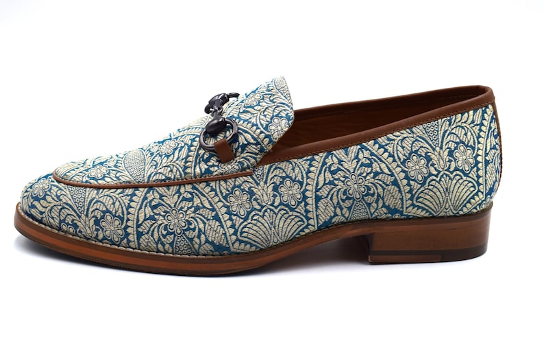 Pode incluir: Sapatos de mocassins azuis e dourados com sola de couro marrom e fivela de metal prateado.