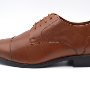 May include: A pair of brown leather lace-up shoes with a cap toe.