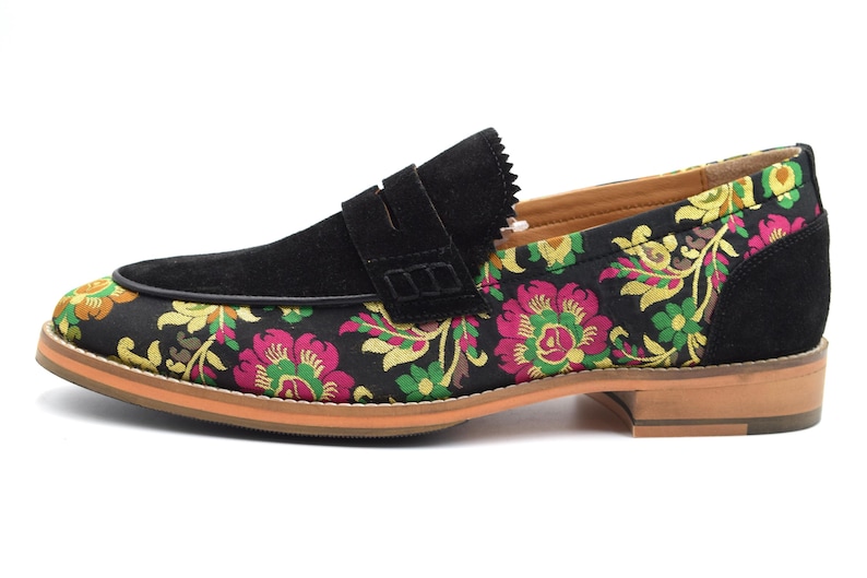 May include: Black suede loafers with a floral pattern on the front and a brown leather sole.