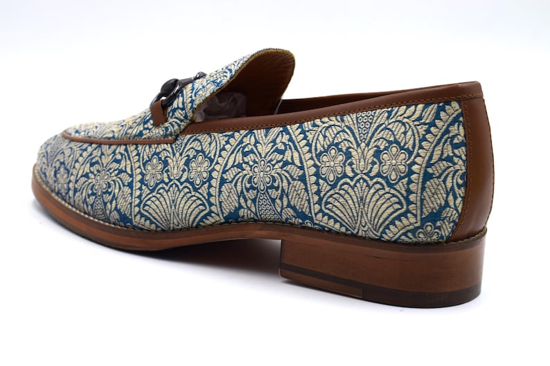Pode incluir: Sapatos de mocassim azuis e dourados com sola de couro marrom e fivela decorativa.