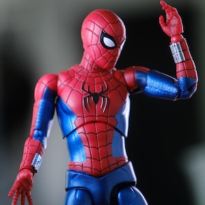 Può includere: Un action figure di Spider-Man rosso e blu con un emblema a ragno nero sul petto, lenti oculari bianche e polsini argentati. Il testo FIGURE NOT INCLUDED IN PURCHASE è visibile nella parte superiore dell'immagine su sfondo scuro.