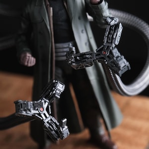 May include: A detailed action figure of a character in a long green coat and sunglasses, with mechanical arms extending from the back. The arms are gray with red accents, and the figure is standing on a wooden surface.