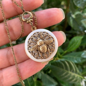 Peut inclure: Un collier avec un médaillon en or orné d'une abeille en émail blanc. L'abeille est entourée d'un motif délicat en filigrane.