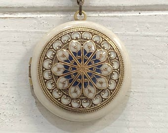 May include: A white and gold locket necklace with a blue and white floral design. The locket has a detailed ornate design around the edge.