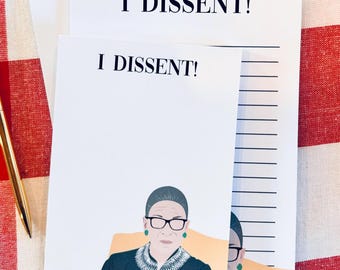 May include: Three white notepads with black lined paper. Each notepad has the text "I DISSENT!" printed on the top. The bottom notepad features a black and white illustration of Ruth Bader Ginsburg.
