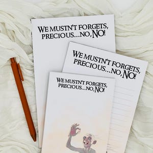 Puede incluir: Tres blocs de notas blancos con el texto "We mustn't forgets, precious...no, no!" impreso en cada uno. El bloc de notas superior es el más grande, el bloc de notas del medio es ligeramente más pequeño y el bloc de notas inferior es el más pequeño. El bloc de notas inferior presenta una ilustración de Gollum del Señor de los Anillos.