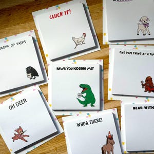 May include: A collection of square white sticky note pads featuring various animal illustrations and humorous text including Cluck It, A Murder of Tasks, Rawr You Kidding Me, One Dam Thing at a Time, Oh Deer, Whoa There, and Bear With Me.