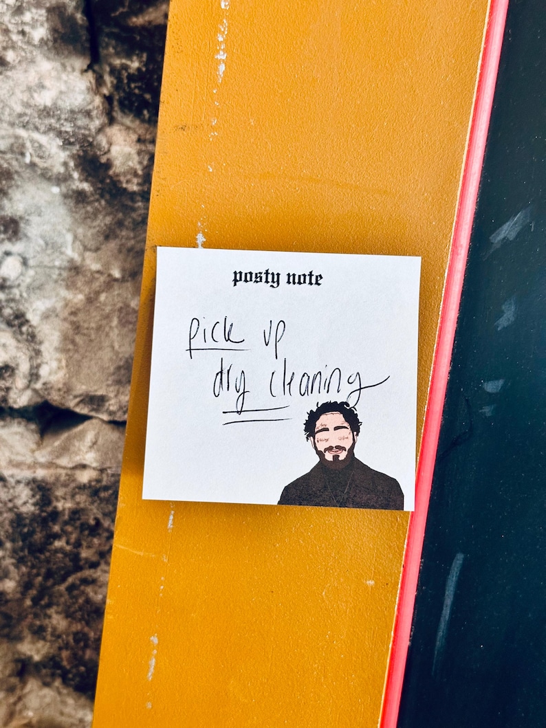 May include: A white sticky note with the text "posty note" at the top. The note says "pick up dry cleaning" in black handwriting. A cartoon illustration of a man with a beard is at the bottom of the note.