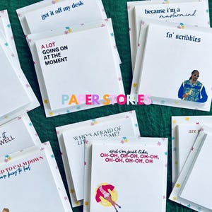May include: A collection of colorful sticky notes with various phrases and illustrations. The notes are arranged on a green surface. Some of the phrases include "A lot going on at the moment", "Remember it all too well", "You need to calm down", "Who's afraid of lit", "And I'm just like oh-oh, oh-oh, oh-oh", "Get it off my desk", "Because I'm a mastermind", "Fo' scribbles", "Are you", "Nu for it?", "Posty note".