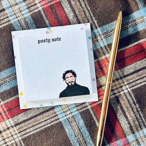 May include: A white notepad with a black and white illustration of a person with a black turtleneck. The notepad has a colorful background with small stars and the text "posty note" at the top.