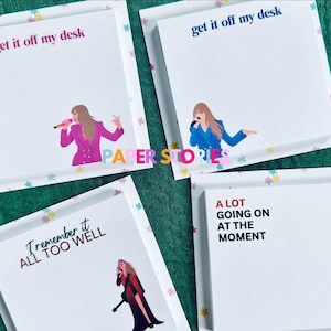May include: Four white sticky note pads with colorful flower borders. The top two pads have the text "get it off my desk" in pink and blue lettering. The bottom left pad has the text "Remember it all too well" in brown lettering. The bottom right pad has the text "A lot going on at the moment" in black lettering.