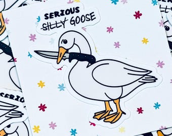 May include: A white goose with a black knife in its beak. The goose is on a white background with a pink, blue, and yellow flower pattern. The text "SERIOUS SILLY GOOSE" is written above the goose.