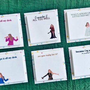 May include: Six white square sticky notes with colorful star borders and black text. Each note features a different lyric from Taylor Swift songs. The lyrics are "get it off my desk", "Remember it all too well", "Who's afraid of little old me?", "get it off my desk", "are you ready for it?", and "because I'm a mastermind".