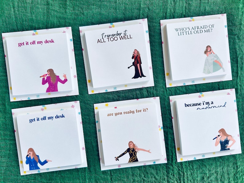 May include: Six white square sticky notes with colorful star borders and black text. Each note features a different lyric from Taylor Swift songs. The lyrics are "get it off my desk", "Remember it all too well", "Who's afraid of little old me?", "get it off my desk", "are you ready for it?", and "because I'm a mastermind".