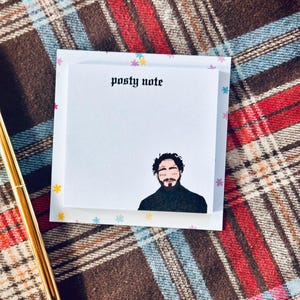May include: A white sticky note with the text "posty note" in black gothic font. A cartoon illustration of a man with a beard and black hair is at the bottom of the note.