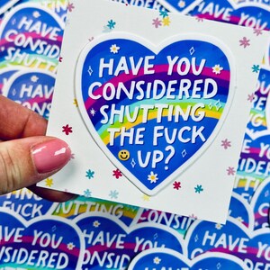 Puede incluir: Una pegatina en forma de corazón con el texto "HAVE YOU CONSIDERED SHUTTING THE FUCK UP?" en blanco, azul y arcoíris. El diseño incluye pequeños motivos florales y estrellas. El fondo presenta pegatinas similares.