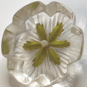 May include: A clear, flower-shaped decorative object with a white center and green accents. The petals are translucent, and the center features a small, white dot. The object has a detailed, carved appearance.