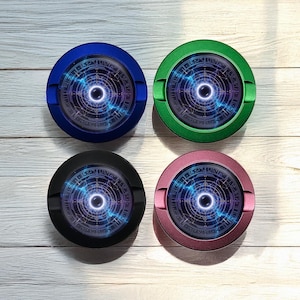 Könnte beinhalten: Vier runde Aschenbecher in Blau, Grün, Schwarz und Rosa. Jeder Aschenbecher hat ein kreisförmiges, kompliziertes Design in der Mitte mit blauen und violetten Akzenten. Die Aschenbecher sind aus Metall.