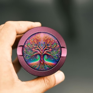 Könnte beinhalten: Ein runder, lilafarbener Metallbehälter mit einem farbenfrohen Lebensbaum-Design. Der Baum ist mit einem Regenbogen an Farben und filigranen Details verziert.