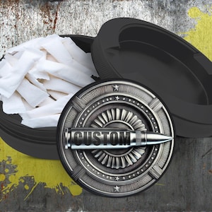 May include: A black metal container with a silver lid featuring a stylized bullet with the word "CUSTOM" on it. The container is filled with white rolling papers.