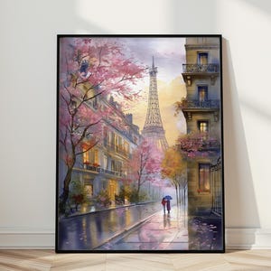 May include: A framed watercolour print depicting a Parisian street scene. The Eiffel Tower is in the background, with buildings lining the street. Pink blossom trees and a couple with an umbrella add colour to the wet street.