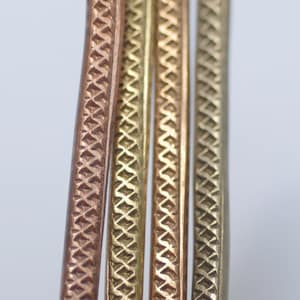 May include: Four metal bangles with a diamond pattern. The bangles are in different shades of gold and copper.