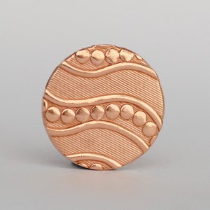 May include: A round, copper-colored button with a wavy design and a row of raised dots along each wave.