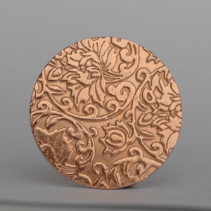 Puede incluir: Un adorno redondo de metal de color cobre con un intrincado diseño floral.