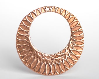 May include: A copper-colored, open-circle pendant with a detailed, leaf-like pattern around the outer edge. The pendant has a small hole at the top for hanging. The design is symmetrical and the metal has a warm, metallic sheen.