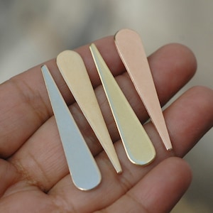 Könnte beinhalten: Vier lange, dünne, spitze Metallstücke in verschiedenen Farben: Silber, Gold, Roségold und Kupfer. Die Stücke sind fächerförmig auf einer Hand angeordnet.