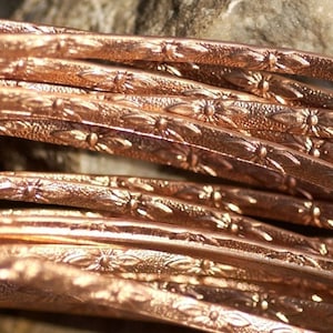 May include: Close-up of a bundle of copper wire with a decorative floral pattern. The wire is shiny and has a warm, reddish-brown colour.