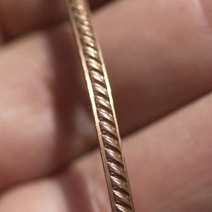 May include: A close-up of a gold-colored metal bangle bracelet with a rope-like design.